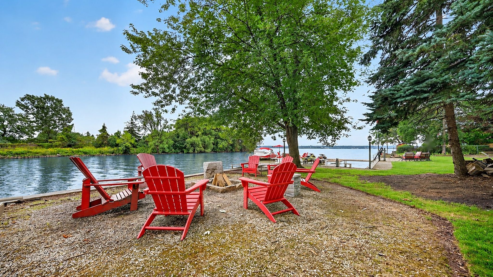 Red Muskoka chairs at the shoreline under the trees