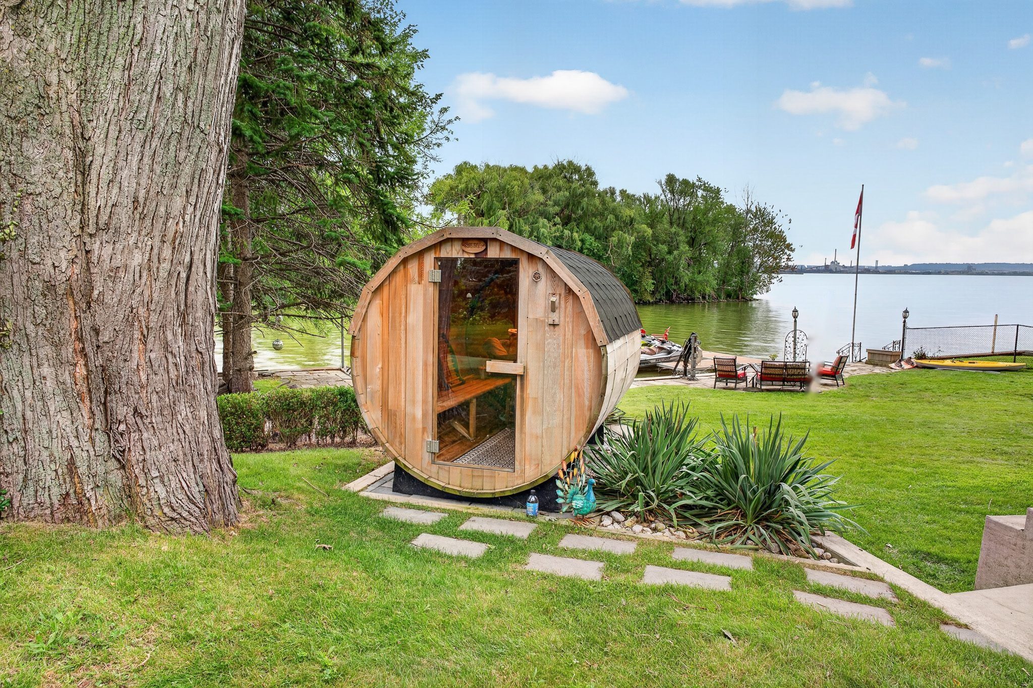 The barrel sauna on the lawn with the bay behind