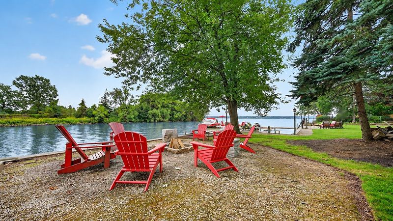 Red Muskoka chairs at the shoreline under the trees